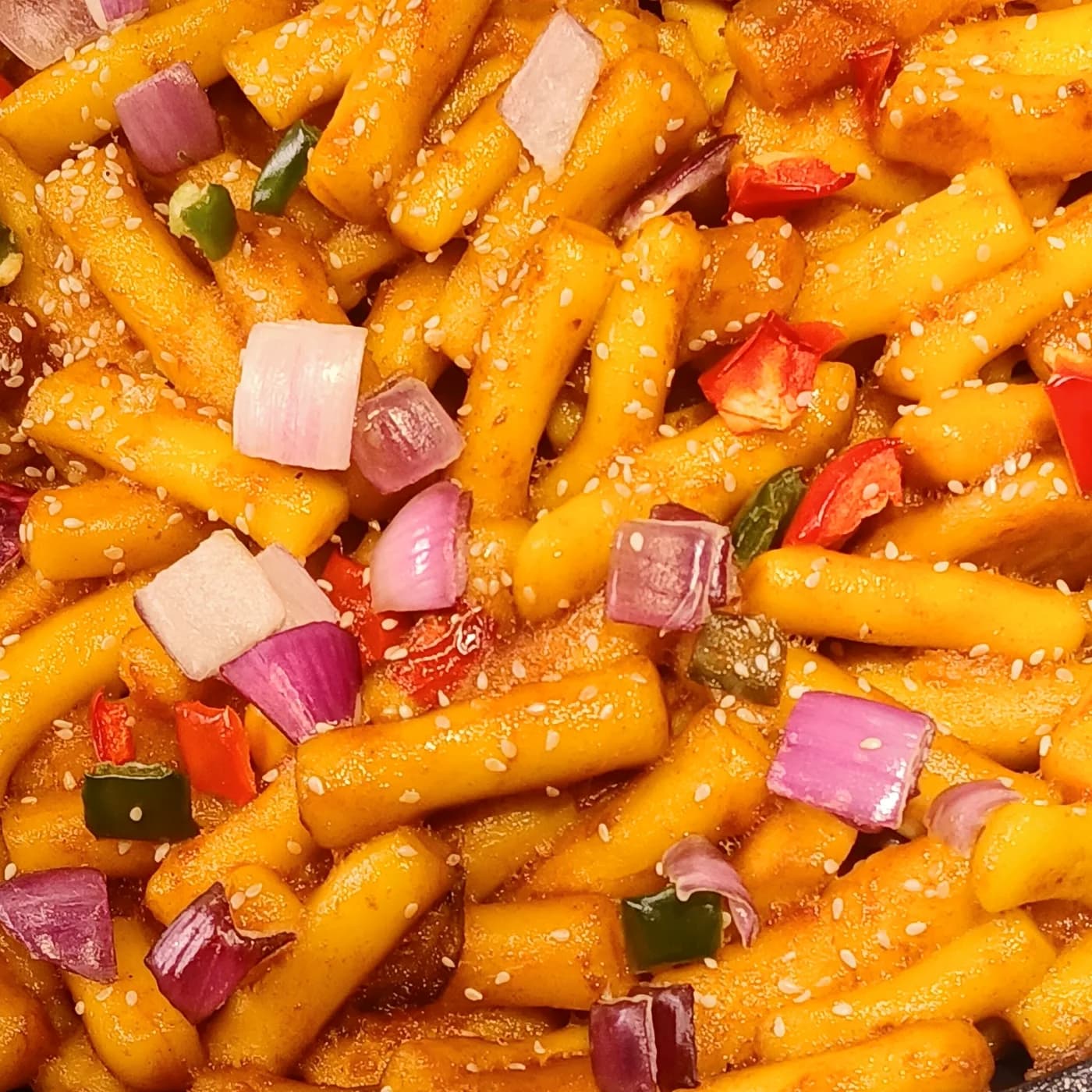 Spicy tteokbokki rice cakes in red-orange sauce with sesame seeds