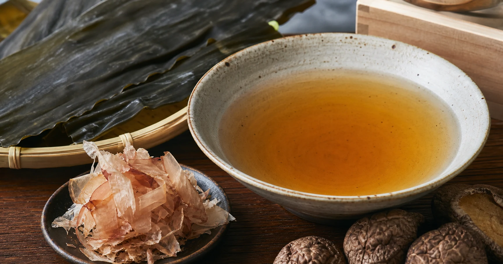 Clear amber dashi broth beside kombu kelp, shaved katsuobushi, and dried shiitake