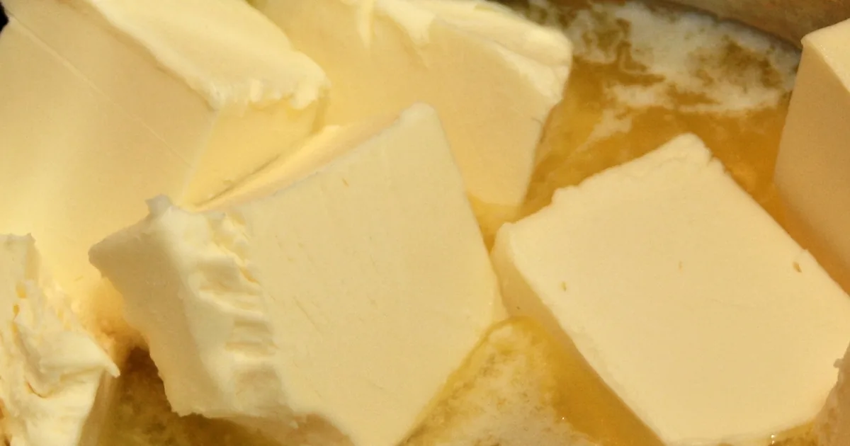 Golden ghee in a brass bowl with a spoon of clarified butter beside whole spices
