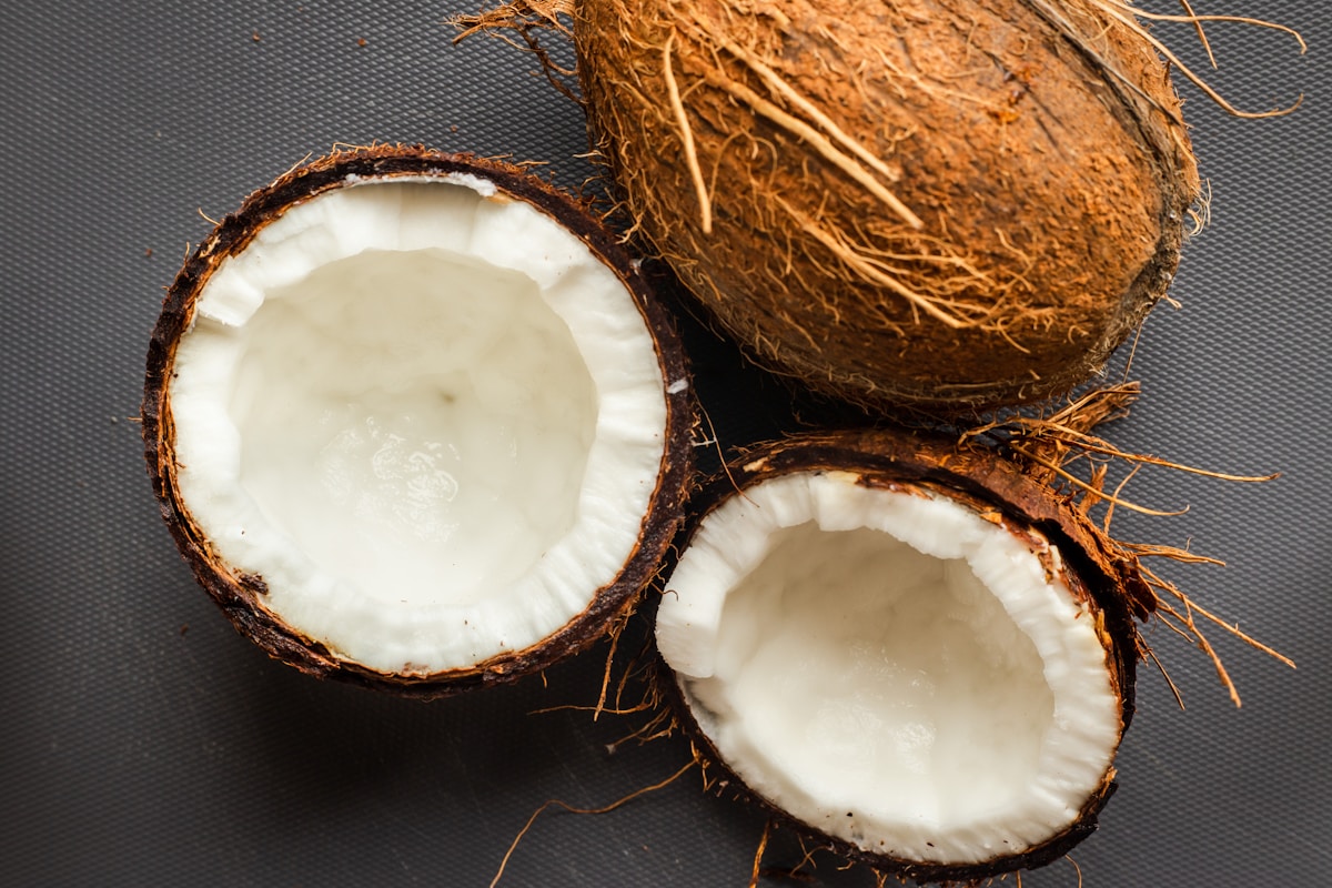 Fresh coconut milk poured beside opened coconuts