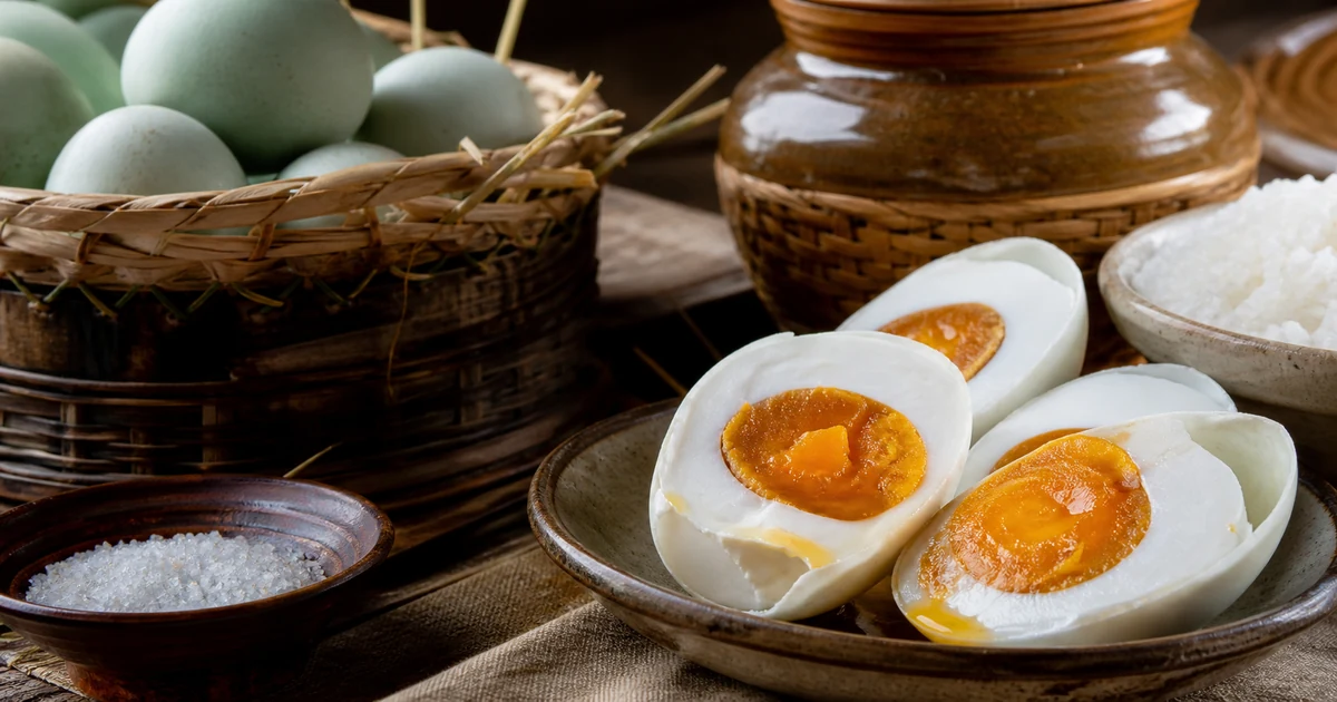 Halved salted duck eggs with firm golden orange yolks beside a brining jar