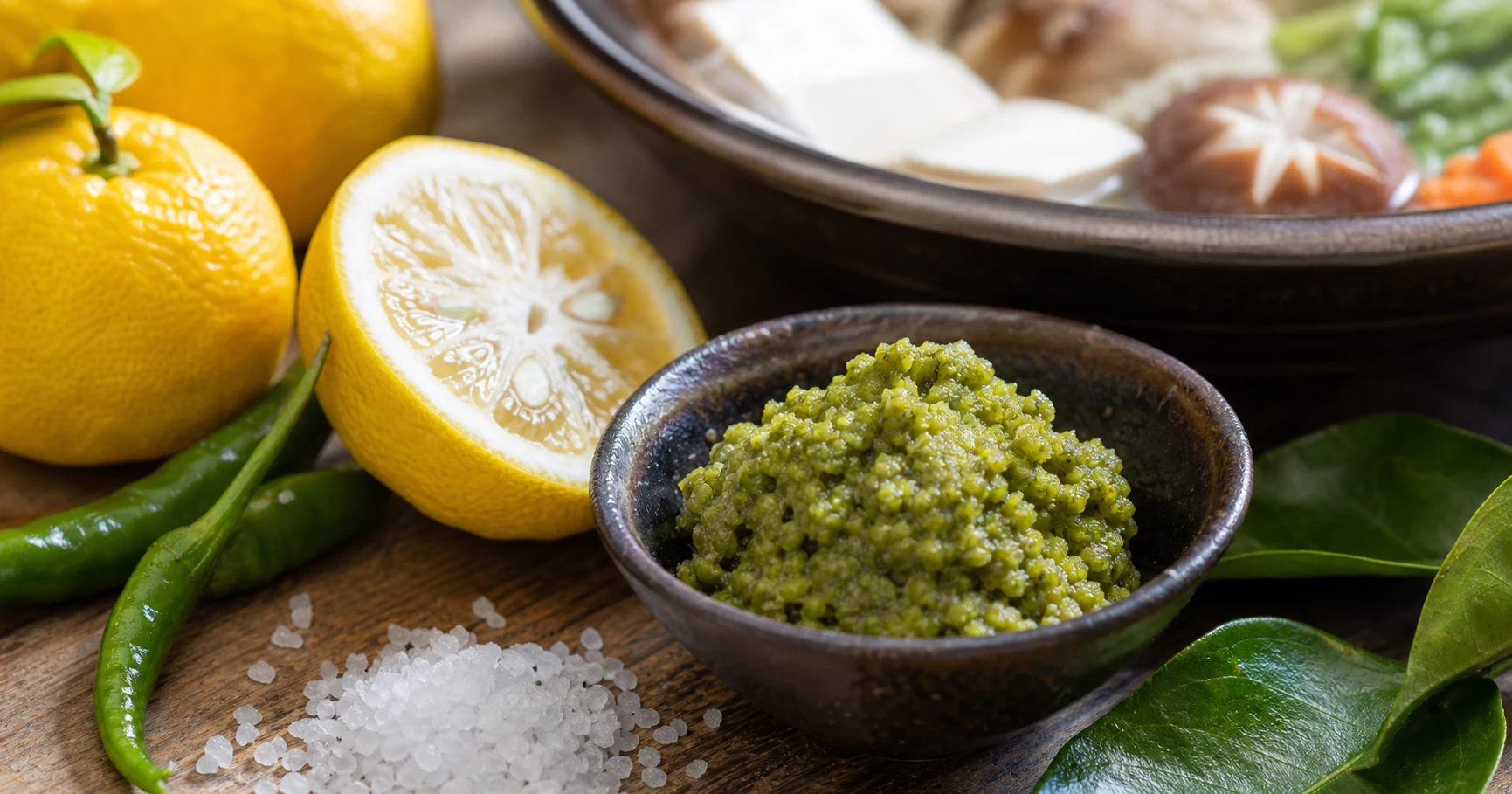 Green yuzu kosho paste beside yuzu citrus, green chilies, and coarse salt