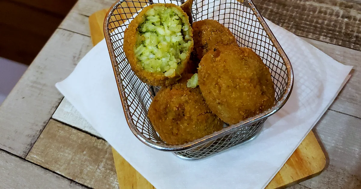 Golden Sicilian arancini cut open to reveal rice, ragù, peas, and cheese