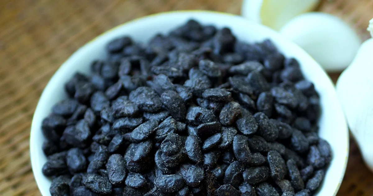 Wrinkled black douchi fermented soybeans beside garlic chili and a clay jar